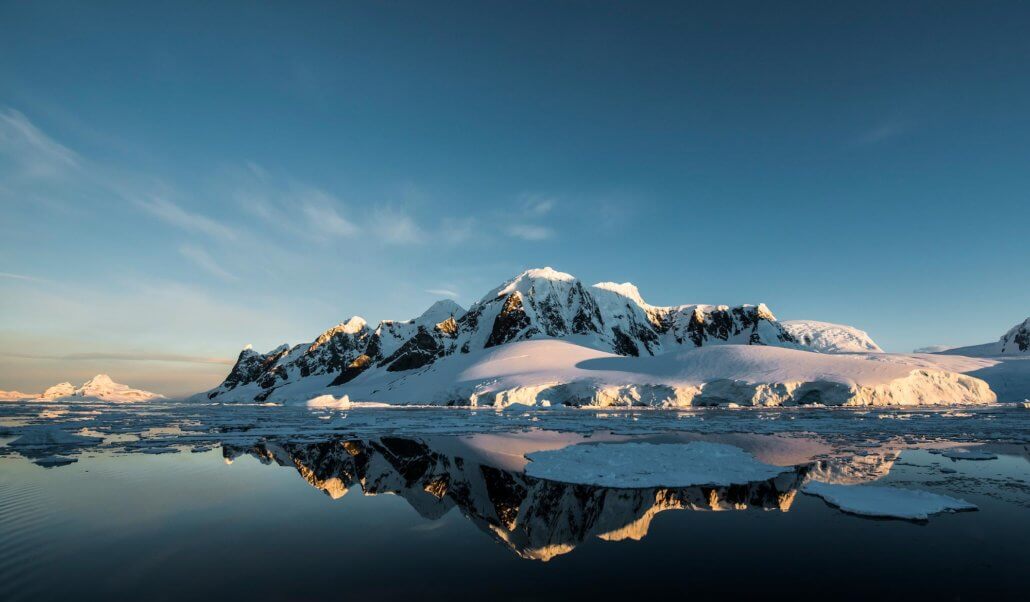 Schneebedeckter Berg vor spiegelglattem Wasser in der Antarktis