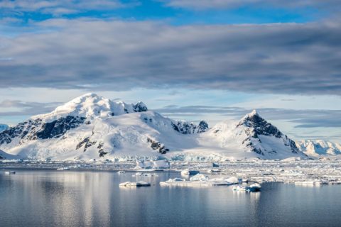 Das ruhige Südpolarmeer mit treibenden Eisschollen und schneebedeckten Bergen von Cuverville Island im Hintergrund