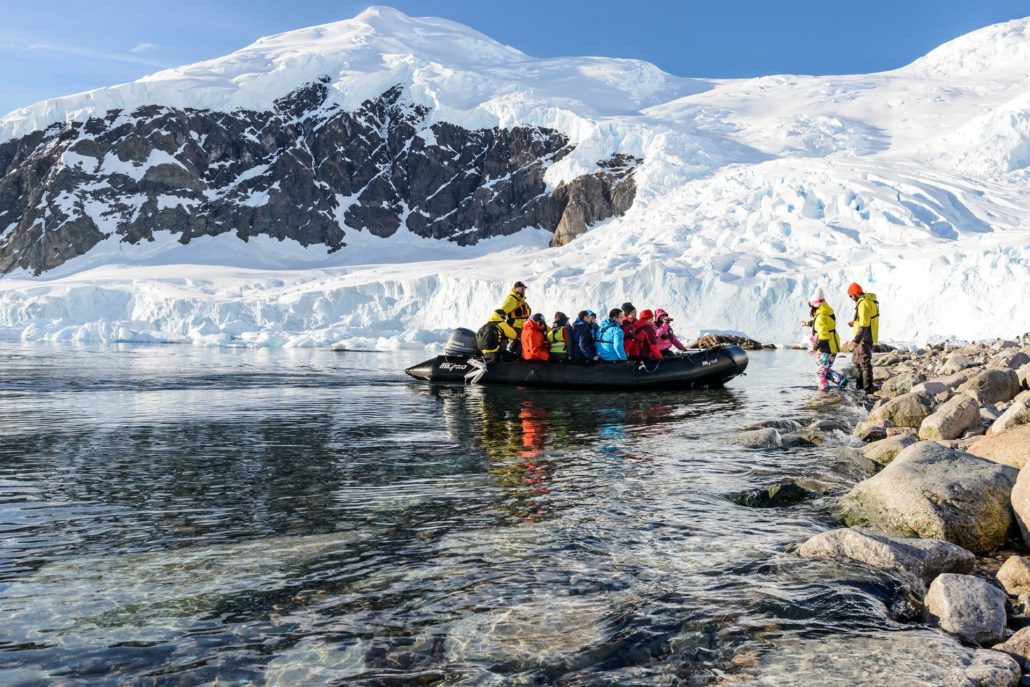 Ein Zodiac-Schlauchboot mit duzenden Reisenden landet auf einer schneebedeckten Insel an