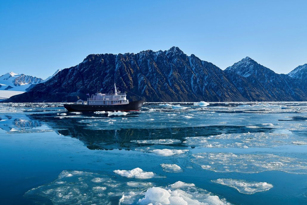 The MS Balto navigates through the drift ice with partially snow-capped mountains in the background