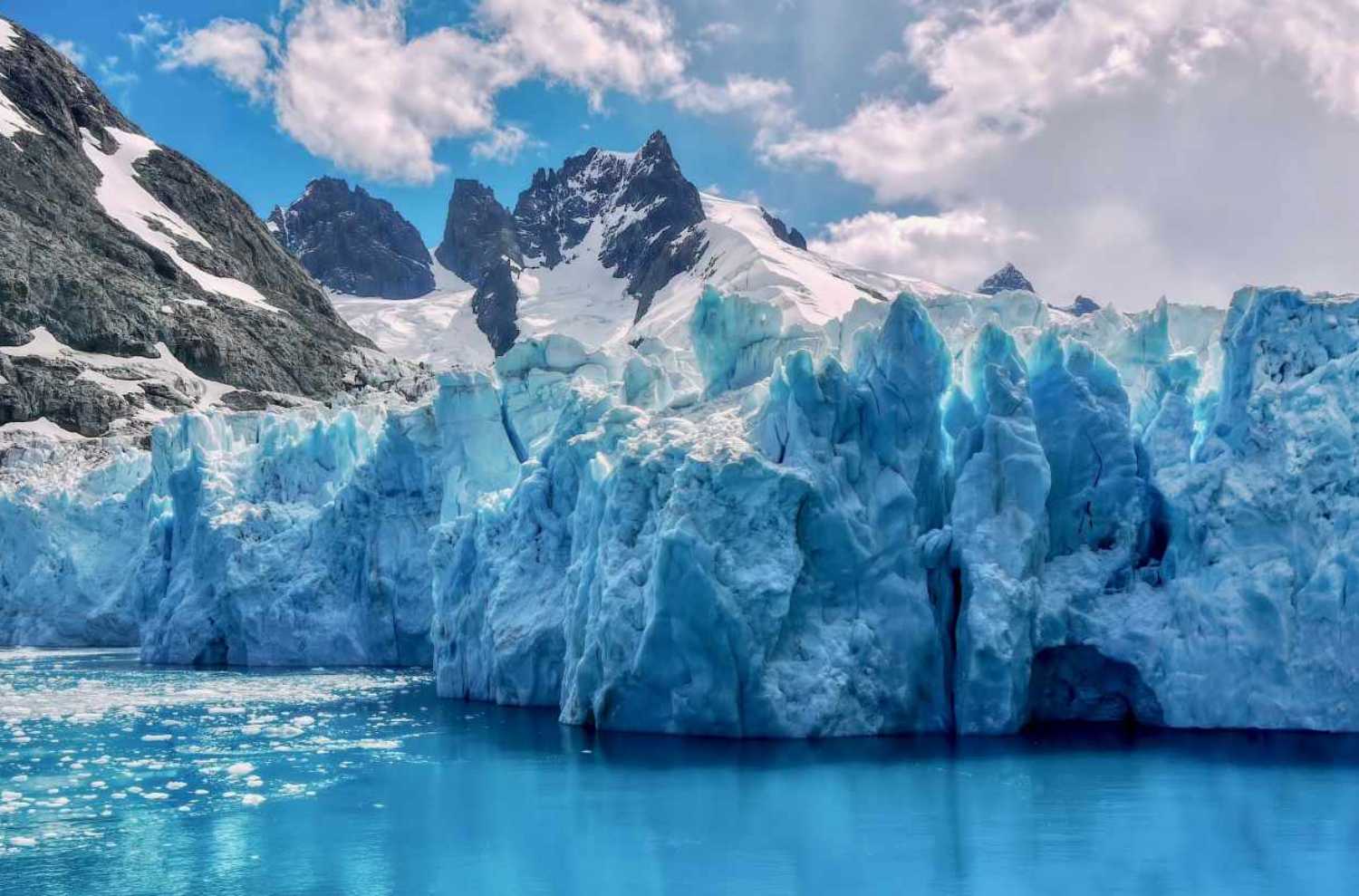Closeup view of the textured surface of a glacier face, with jagged, snowcapped mountains in the background, in the Drygalski Fjord of South Georgia Island in the South Atlantic Ocean. Drygalsky Fjord