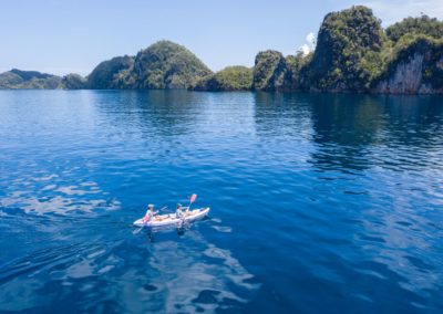 Kayakers paddle across the blue sea and explore the amazing limestone islands that rise from the Raja Ampat seascape.
