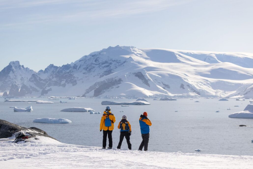 Drei Menschen in antarktischer Landschaft blicken aufs Meer