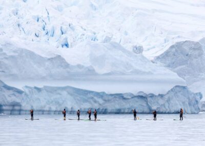 Mehrere Stand Up Paddler vor einer Landschaft aus Eis