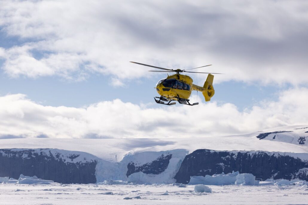Gelber Helikopter fliegt über Polarlandschaft