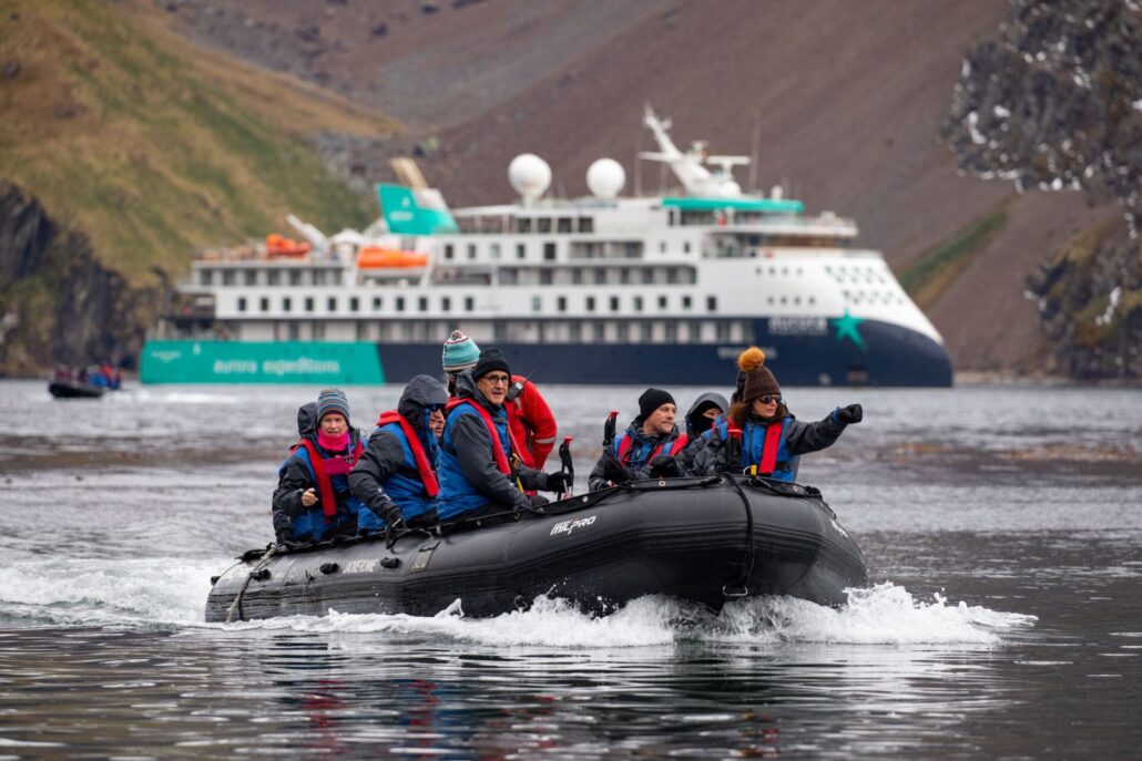 Ein Zodiac mit mehreren Insassen fährt über das Meer, im Hintergrund ein Expeditionsschiff