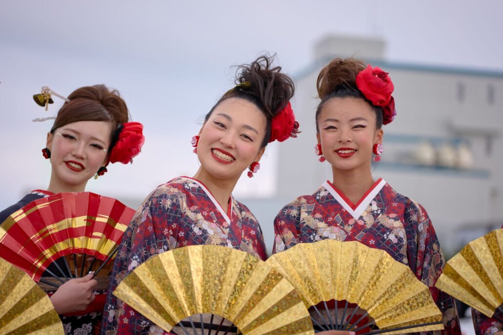 Drei japanische junge Frauen mit hochgesteckten Haaren, traditionellen Gewändern und goldenen Fächern