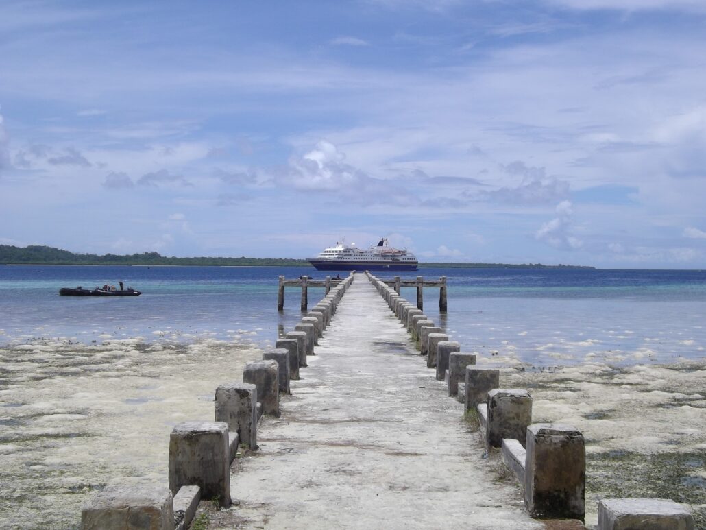 Ein langer Steg führt aufs Meer zu, auf dem Wasser im Hintergrund ein Expeditionsschiff