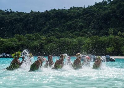 Mehrere Menschen plantschen in flachem Wasser vor einem Strand
