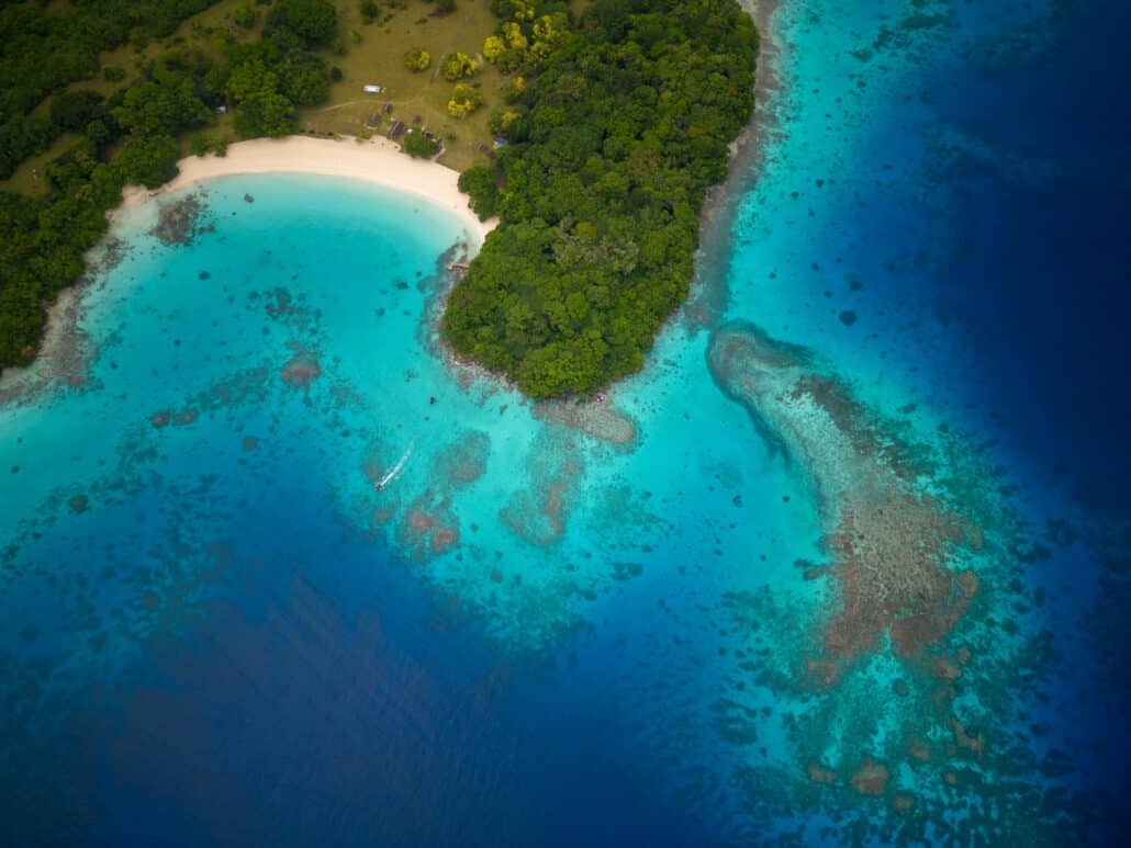 Eine Insel von oben, umgeben von türkisfarbenem bis dunkelblauem Meer