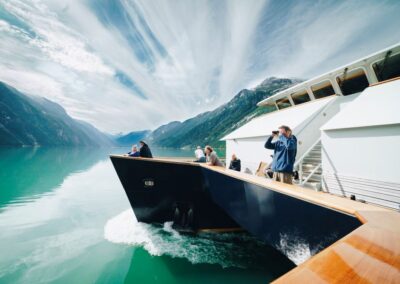 Ein Mann steht auf der Seite eines Schiffs und blickt mit dem Fernglas in Richtung Küste.