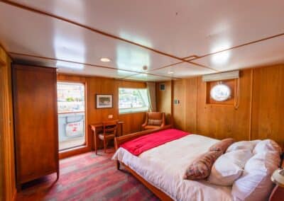 Kabine mit Bett, Schreibtisch und Sessel sowie Glastür auf das Deck des Schiffes