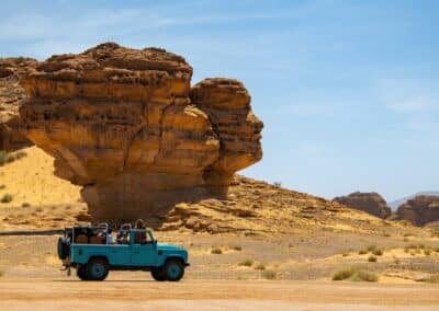 Ein türkisfarbener Jeep steht vor einer Felsformation mitten in der Wüste
