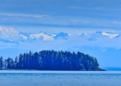 Landschaft mit Wasser, Wald und schneebedeckten Bergen dahinter