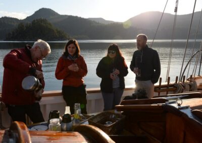 Vier Menschen stehen an Bord eines kleinen Schiffes vor Naturkulisse und trinken etwas.
