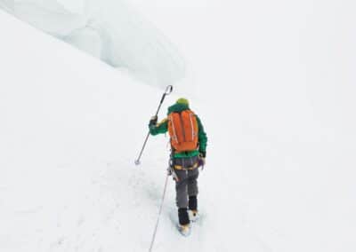 A man in winter clothing and carrying a backpack trudges through deep snow.