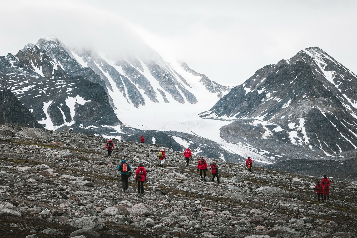 Wandergruppe auf einer Anhöhe mit Blick auf einen Gletscher in Spitzbergen