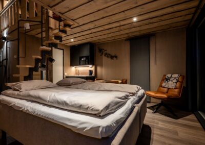 Double bed, with a small kitchen in the background and a staircase leading up to the loft area