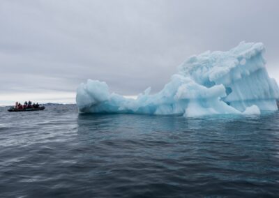 Blauer Eisberg am Packeisrand, daneben ein Zodiac mit Expeditionsgästen