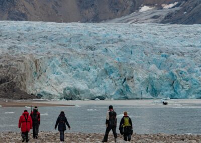 Wandergruppe an einem Strand vor einer großen Gletscherwand auf Spitzbergen