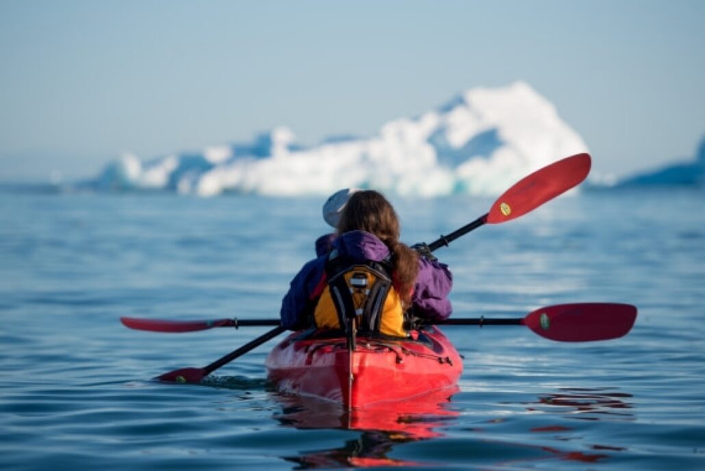 A kayaker in front of an iceberg in Arctic waters