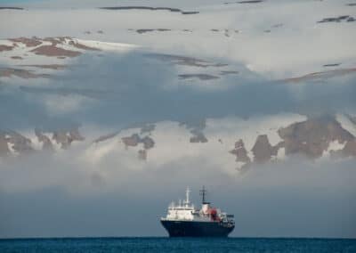Expeditionsschiff MS Ortelius klein vor dramatischer Tundra-Bergkulisse mit Wolken, Nordspitzbergen