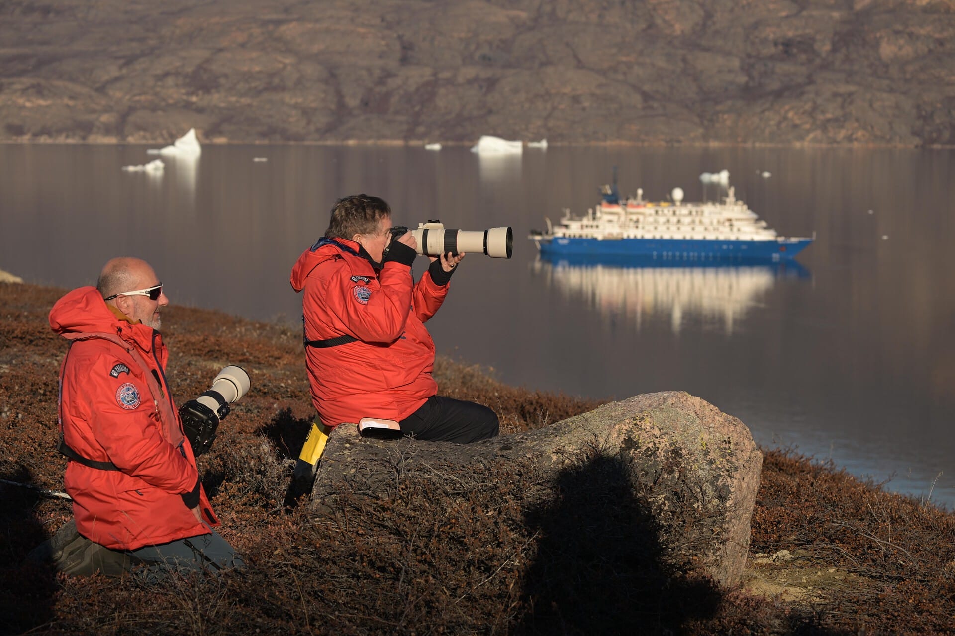 Expeditionsfotografen mit Teleobjektiv vor Expeditionsschiff im Fjord