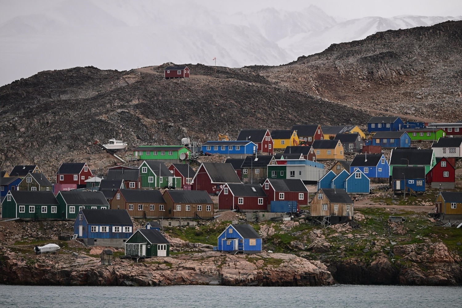 Bunte Holzhäuser der Inuit-Siedlung Ittoqqortoormiit am Berghang