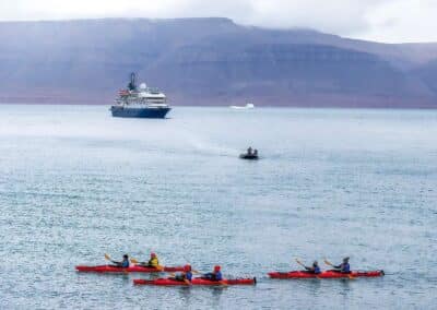 Vier rote Kajaks im Fjord vor Expeditionsschiff in Ostgrönland