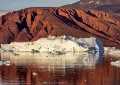 Roter Sandsteinberg mit Eisberg im Fjord am Scoresbysund