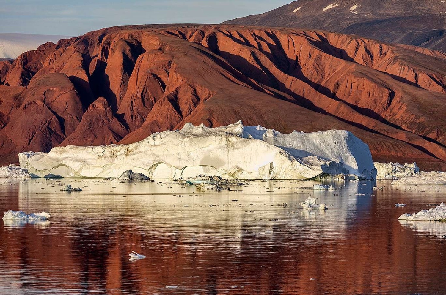 Roter Sandsteinberg über Eisberg im Scoresbysund-Fjord