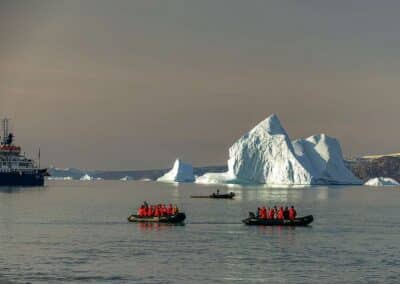 Expeditionsschiff und zwei Zodiacs vor Eisbergen am Fjord