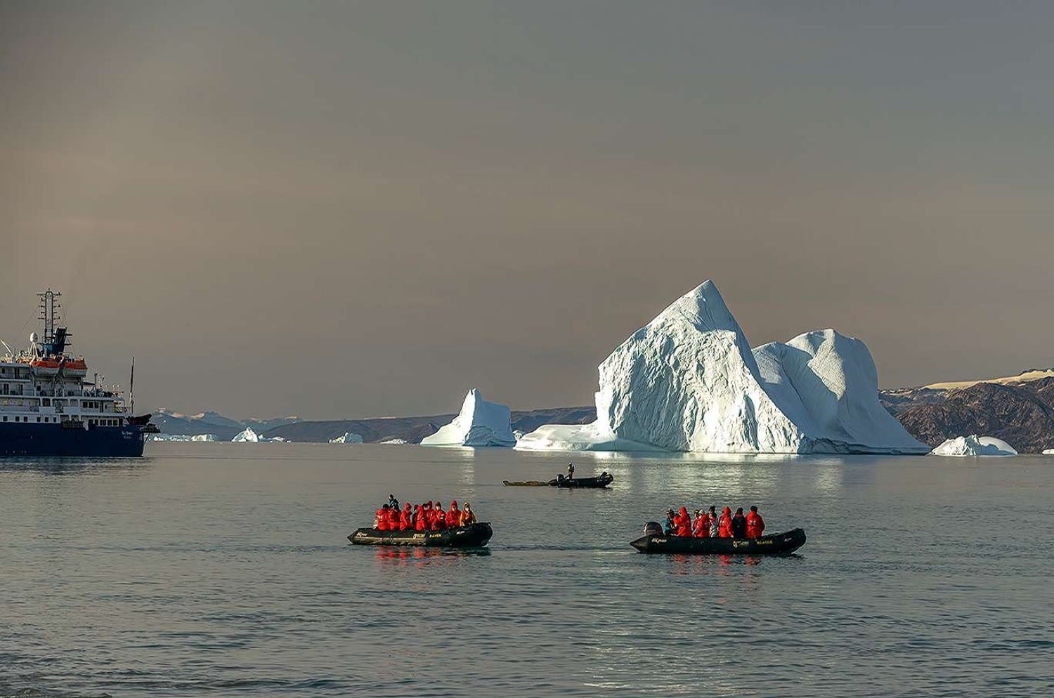 Expeditionsschiff und zwei Zodiacs vor Eisbergen am Fjord