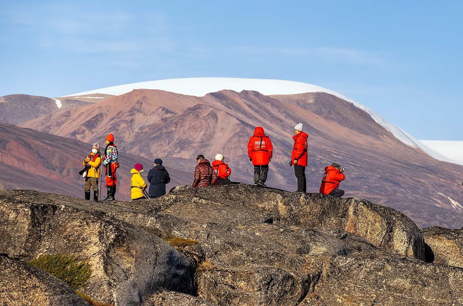 Wandergruppe auf Felsplateau mit schneebedecktem Bergpanorama