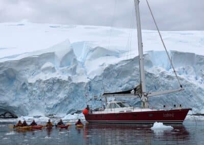Gruppe Kajaks vor der Polar-Segelyacht und einer Gletscherwand in der Antarktis