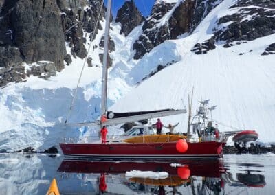 Eselspinguine an einem Strand mit der ankernden Polar-Segelyacht im Hintergrund