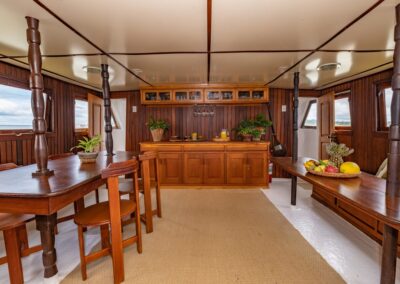 The Tupaiú's wood-paneled dining room, featuring a long table, a buffet, and windows overlooking the river