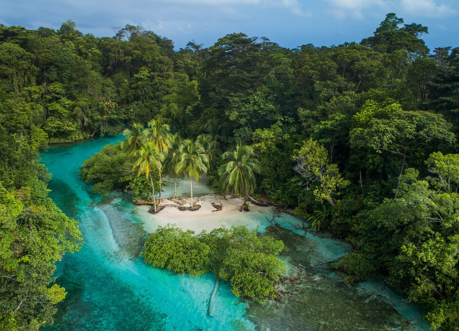 Türkise Bucht mit kleinem Sandstrand zwischen dichtem Regenwald aus der Luft