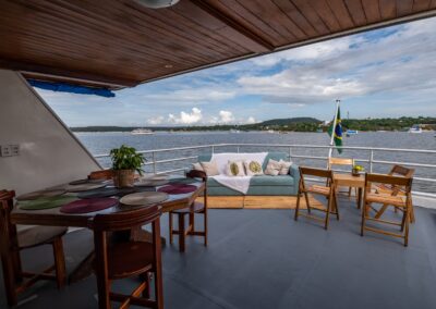 The Belle Amazon's covered veranda with a dining table, sofa, and a view of the river