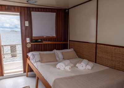 Double cabin on the Tupaiú with a double bed, wood paneling, and a window overlooking the river