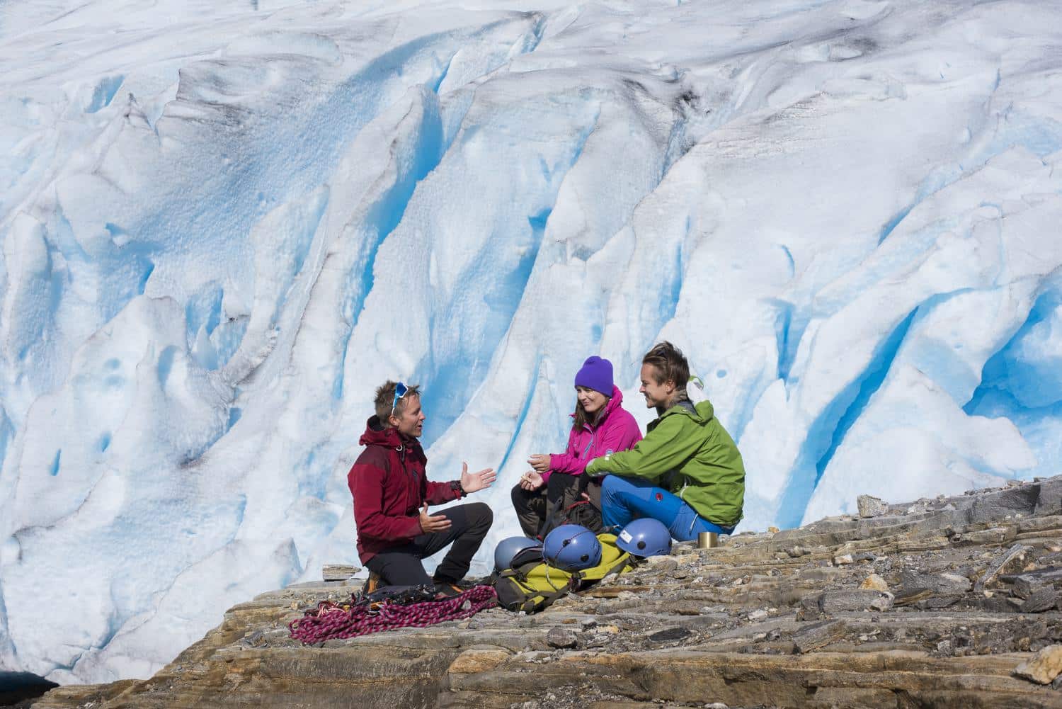 Vor der blauen Wand des Svartisen Guide und zwei Gäste sitzen mit Seil und Helmen vor der blauen Eiswand des Svartisen