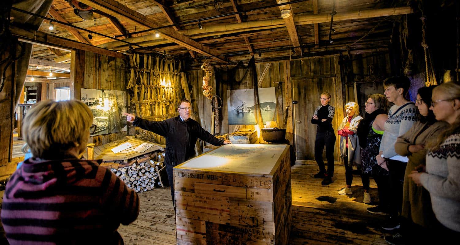 Der Guide erzählt vom Kaufmann und seinen Fischern Guide erzählt einer Reisegruppe im Obergeschoss des alten Kaufladens von Støtt