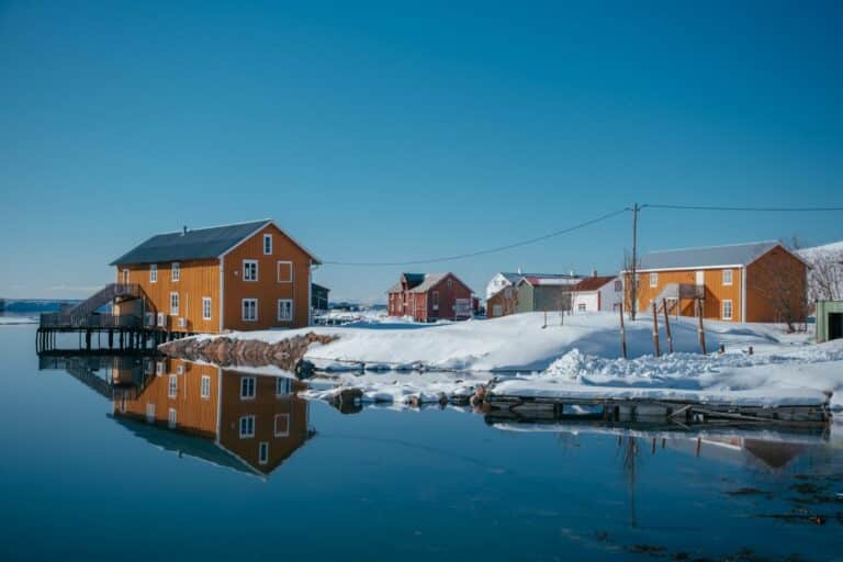 Gelbe und rote Speichergebäude des Handelspostens Støtt spiegeln sich im winterlichen Wasser