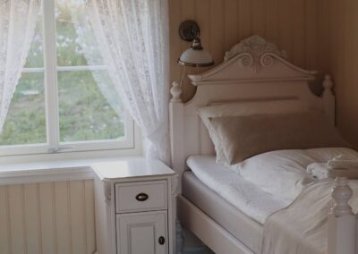 Weiß gestrichenes Schlafzimmer mit antikem Bettgestell und Spitzengardine auf Støtt