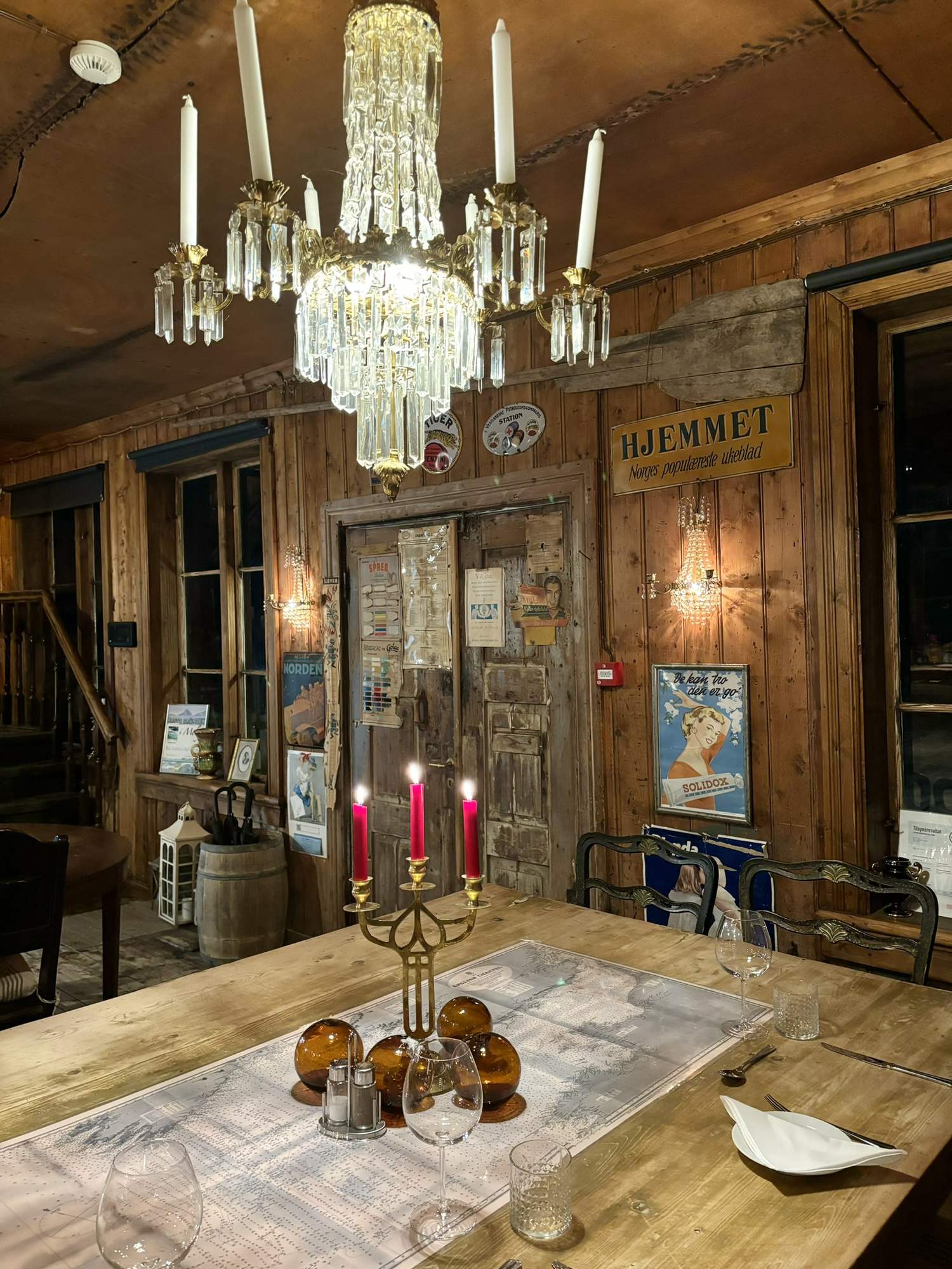 Lange Holztafel mit Messing-Kandelaber unter zwei Kristalllüstern im alten Kaufladen, an den Wänden historische Reklameschilder