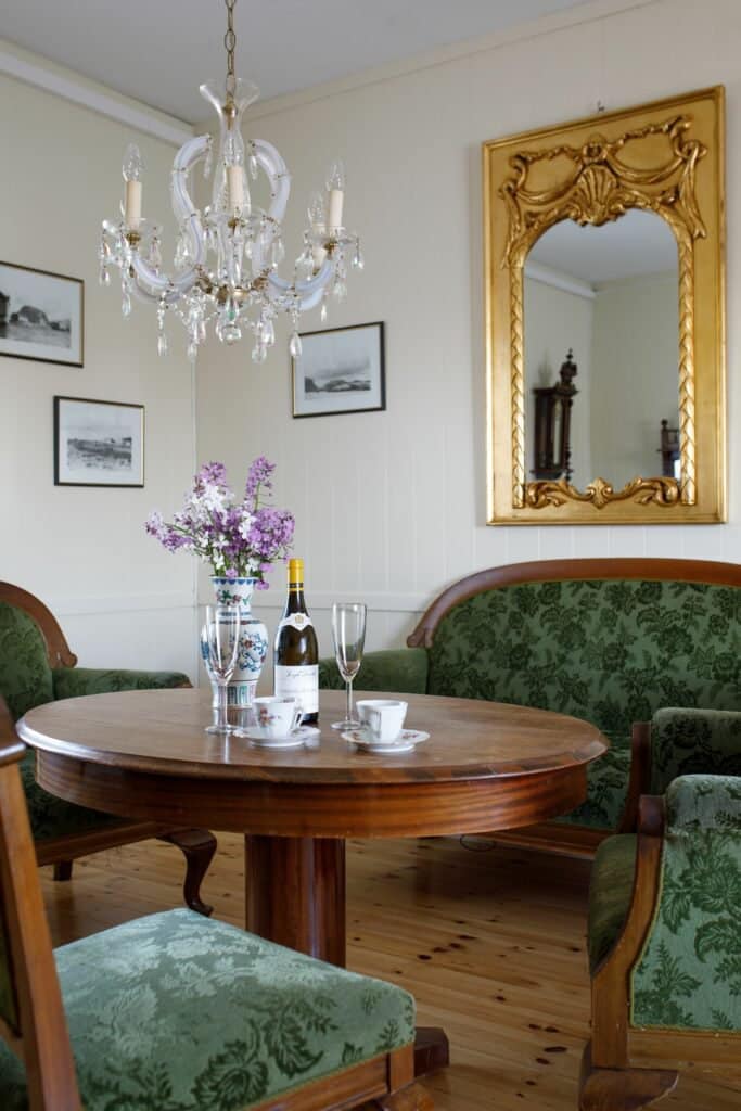 Wohnzimmer eines der Häuser auf Støtt mit Kristalllüster, Goldspiegel, rundem Tisch und gepolsterten Stühlen