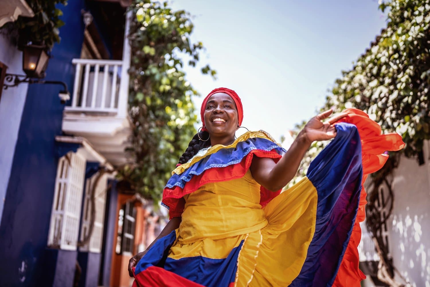 Palenquera mit wehendem Rock in den Farben Kolumbiens A smiling woman in a yellow, blue, and red traditional costume in a colonial alley