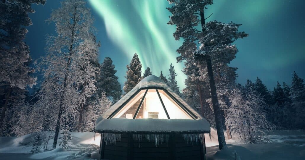 Beleuchtetes Glas-Iglu in Finnland unter grünen Nordlichtern im Resort
