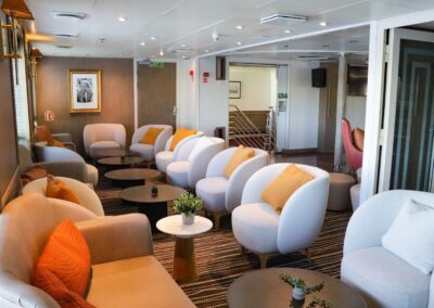 Main Lounge der MS Discoverer mit hellen Sesseln, orangefarbenen Kissen und Bar