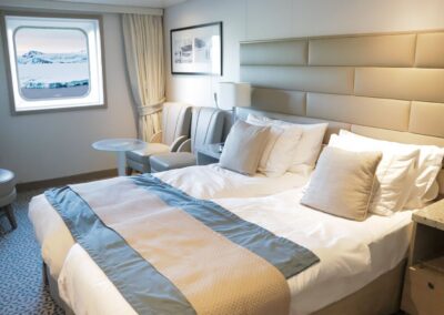 Ocean Kabine der MS Discoverer mit Doppelbett, Sitzecke und Panoramafenster mit Blick auf Schnee und Berge